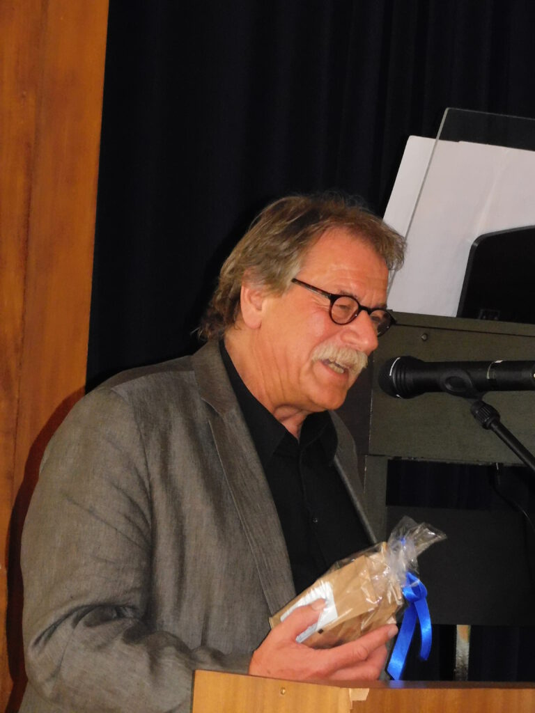 Josef Adrian vor einem Rednerpult mit einem Geschenk in der Hand