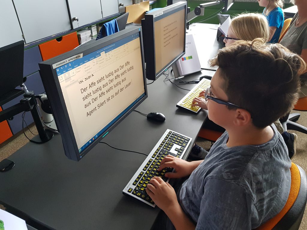 Mehrere Kinder sitzen am PC und lernen das Tastschreiben.