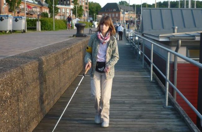 Eine junge Frau mit Langstock läuft über eine Brücke