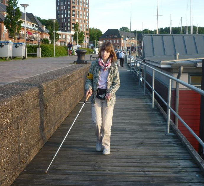 Eine junge Frau mit Langstock läuft über eine Brücke