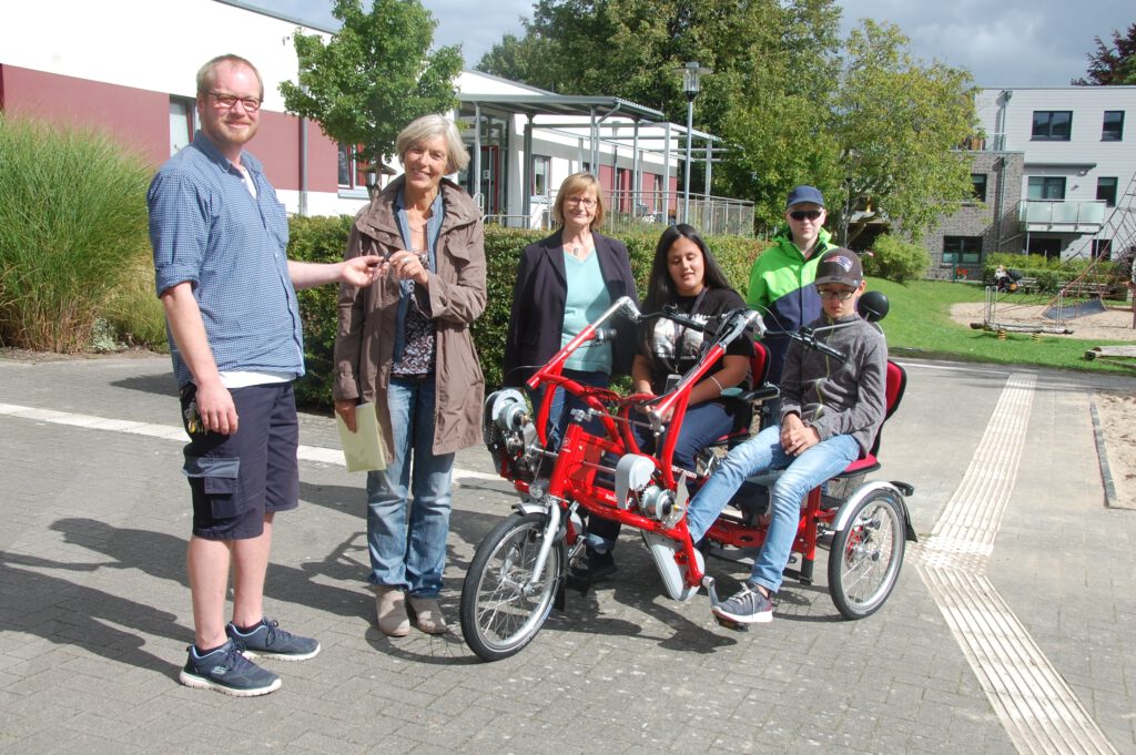 Übergabe des Schlüssels durch Jan Kröger (Vereinsvorsitzender) an Ute Hölscher (stellv. Leitung). Zu sehen sind zudem drei Schüler mit Marion Ewald, einer Mitarbeiterin aus dem Kursteam.Eine Schülerin und ein Schüler sitzen auf einem elektrischen Zweisitzertandem.