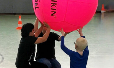Drei Schüler halten in der Turnhalle kniend einen großen Ball in die Höhe.