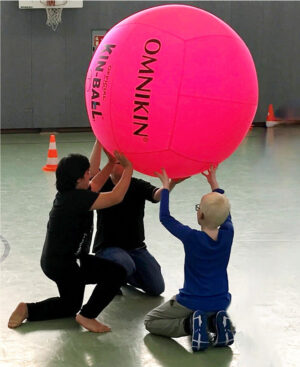 Drei Schüler halten in der Turnhalle kniend einen großen Ball in die Höhe.