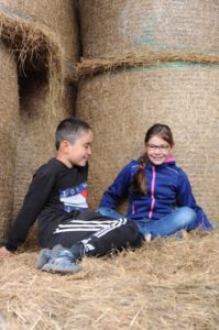 Eine Schülerin und ein Schüler sitzen vor mehreren aufeinandergestapelten Rundballen.