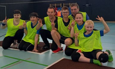 5 Schülerinnen und Schüler sowie zwei Lehrkräfte des LFS sitzen nebeneinander auf dem Hallenboden und schauen in die Kamera.
