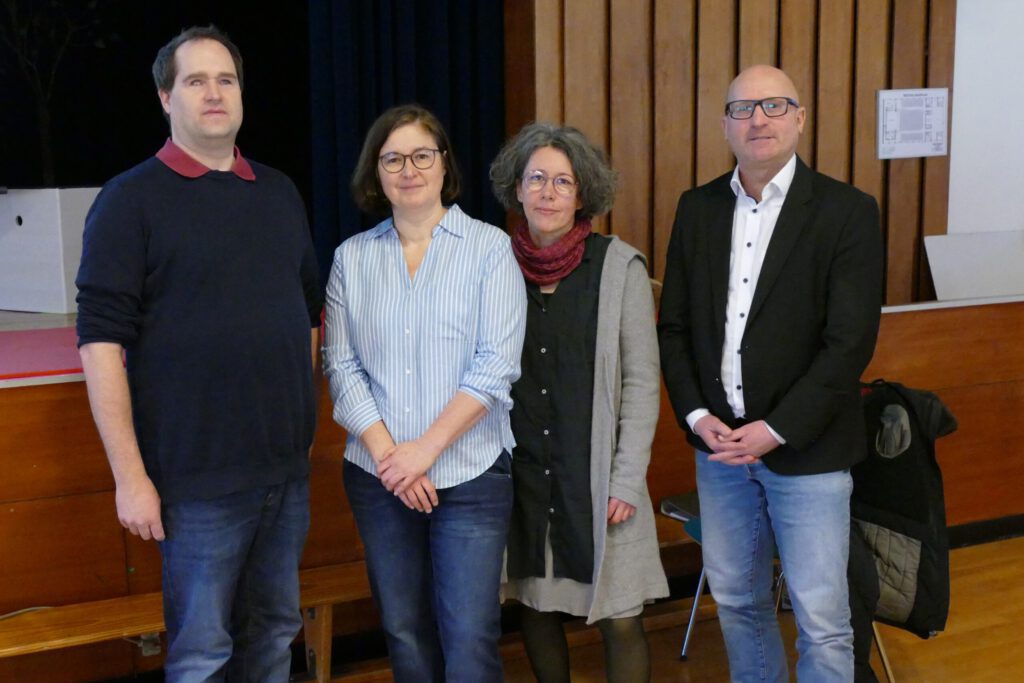 Vier Personen schauen in die Kamera; von links nach rechts: Björn Albrecht, Katharina Bossard De Paz, Nicole Hinsch-Tönnies, Herr Brodersen, im Hintergrund ein Ausschnitt einer Aula.