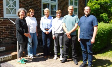 Auf dem Bild sind von links nach rechts: Nicole Hinsch-Tönnies, Katharina Bossert De Paz, Michaela Pries, Lou B., Moritz Magnussen, Björn Albrecht Im Hintergrund sieht man einen Ausschnitt eines roten Backsteingebäudes, das Verwaltungsbebäude des LFS sowie grüne Büsche.