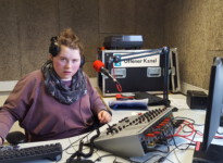 Mit dem Kopfhörer kann ich kontrollieren, wie lange die Musiktitel noch laufen und mit der Tastatur lade ich die Musikjingles in ein spezielles Programm ein, diese werden mir dann über die Sprachausgabe per Kopfhörer angesagt. Schülerin mit Hand auf der Tastatur und auf dem Mischpult