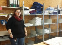 Auf dem Bild sieht man Anna vor einem großen Wäscheregal. Es ist mit großen Ziffern beschriftet, damit sie die fertige Wäsche für die Kunden richtig einsortieren kann.