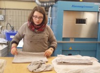 Im nächsten Schritt faltet Anna das Handtuch auf dem Tisch liegend. Anna hat gelernt nach einem gleichbleibenden System zu arbeiten, damit die Handtücher exakt gestapelt werden können. junge Frau faltet Handtücher zusammen