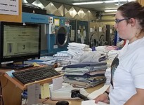 Jedes Wäschestück hat einen Code, den Anna einscannt wird. Die Nummer für das Regalfach wird ihr vergrößert auf einem Bildschirm angezeigt. Danach kann Anna die Wäsche in das richtige Fach einsortieren. junge Frau codiert Wäsche