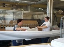Nach einer eingeübten Systematik wird das Laken gemeinsam gefaltet. Im Hintergrund des Bildes sieht man die große Industriemangel.