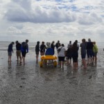 Eine Gruppe von Schüler*innen und Lehrkräften auf einem Watt-Strand.