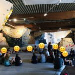 Eine Schüler*innen-Gruppe sitzt in einer Boulder/Kletter-Halle.