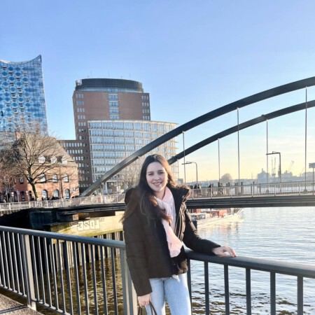 Julia steht an den Hamburger Landungsbrücken, lächelt in die Kamera. Im Hintergrund die Elbe und das Konzerthaus, die Elbphilharmonie, kurz Elphi.