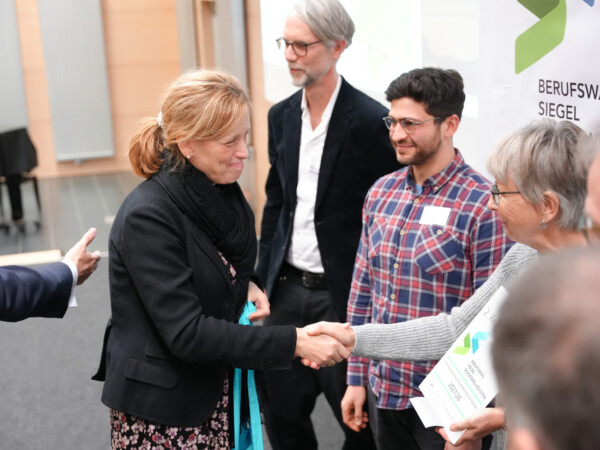 Karin Prien schüttelt lächelnd die Hand von Frau Brodersen (LFS), die eine Urkunde mit dem Berufswahlsiegel hält.