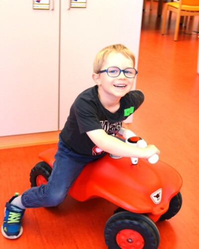 Ein fröhlicher Junge fährt im Kurshaus des LFS auf einem roten Rutschauto