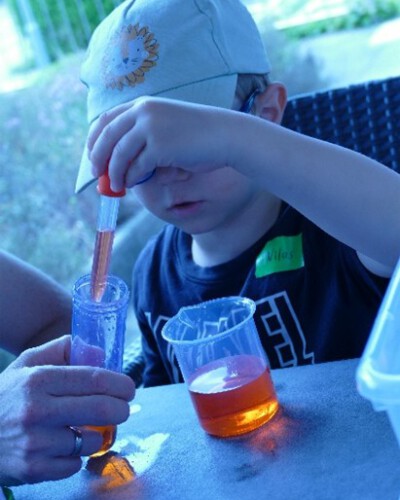 Ein Kind hält eine Pipette über ein Glas und untersucht orange Flüssigkeit bei einem Experiment.
