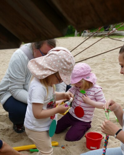Kinder spielen mit ihren Eltern im Sand und fädeln bunte Perlen auf