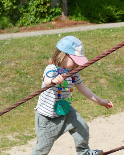 Ein Kind balanciert auf einem Seil und trägt buntes selbstgebasteltes Spielzeug mit sich.