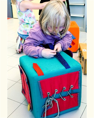 Ein Kind ertastet einen bunten Würfel mit Schnürungen