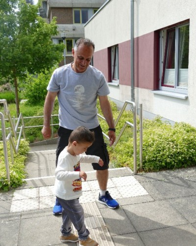 Ein Vater begleitet seinen Sohn beim Gehen auf einem taktilen Leitstreifen vor dem Landesförderzentrum Sehen, Schleswig.