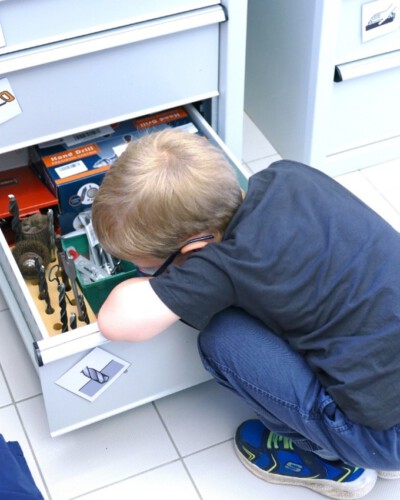 Ein Kind untersucht eine geöffnete Schublade mit Werkzeugen und Materialien.